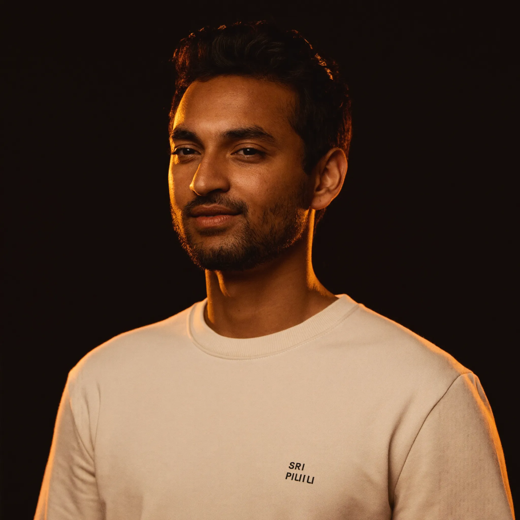 Portrait of Arjun, a South Asian cohort coach who runs $2K cohorts twice a year, wearing a cream FantoClient sweatshirt with warm rim light