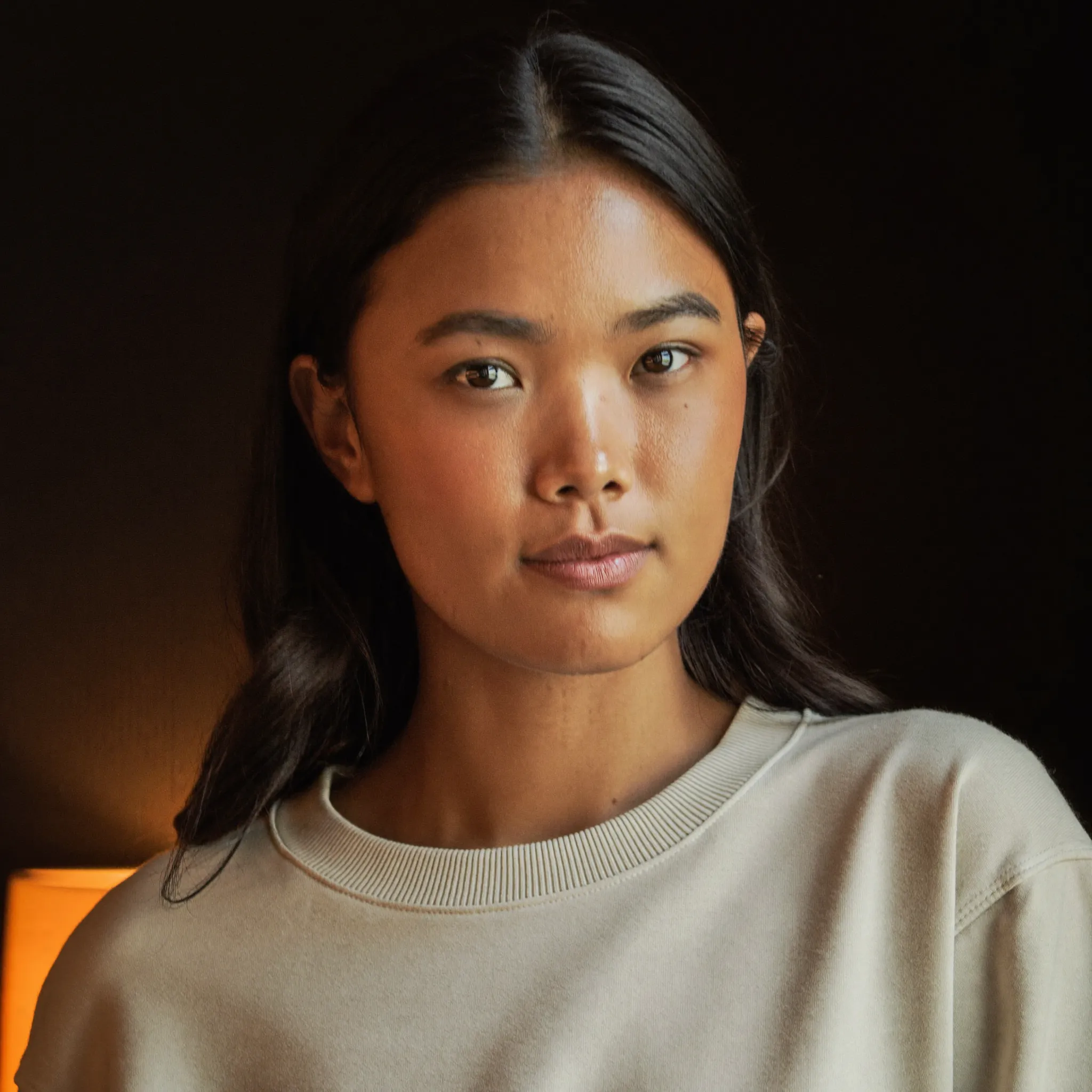 Portrait of Asha, a mixed Asian e-commerce founder and DTC brand owner wearing a cream FantoClient sweatshirt with warm rim light